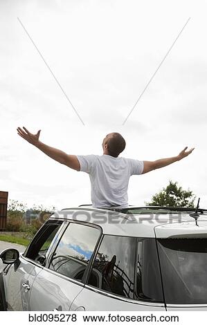 Stock Photo - Hispanic man with arms outstretched standing in sun roof. Fotosearch