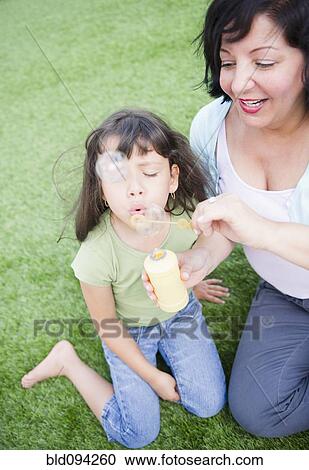 Stock Image - Hispanic mother and daughter blowing bubbles. Fotosearch