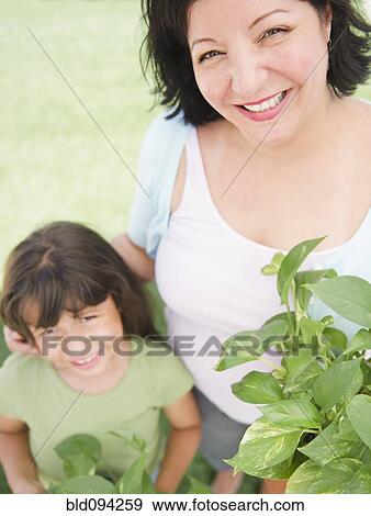 Stock Photo - Hispanic mother and daughter holding plants. Fotosearch
