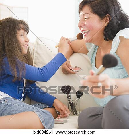 Stock Image - Hispanic mother and daughter putting on makeup. Fotosearch