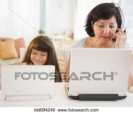 Stock Photo - Hispanic mother and daughter using laptops. Fotosearch