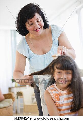 Stock Photo - Hispanic woman brushing daughter's hair. Fotosearch