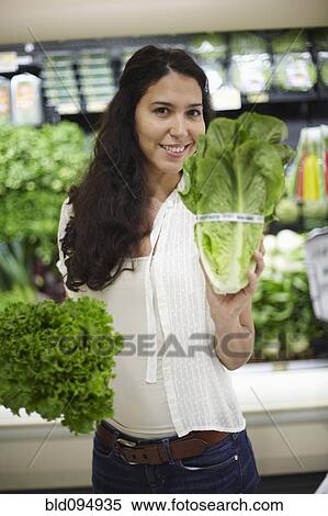 Stock Photography - Hispanic woman holding lettuce in grocery store. Fotosearch