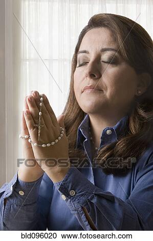 Stock Image - Hispanic woman holding rosary praying. Fotosearch