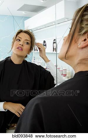 Stock Photo - Hispanic woman looking at reflection in beauty salon. Fotosearch