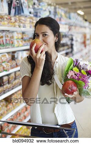 Stock Image - Hispanic woman smelling fruit in grocery store. Fotosearch