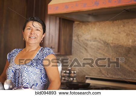 Stock Image - Hispanic woman standing in kitchen. Fotosearch