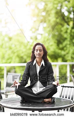 Stock Photo - Indian businesswoman practicing yoga on tabletop. Fotosearch