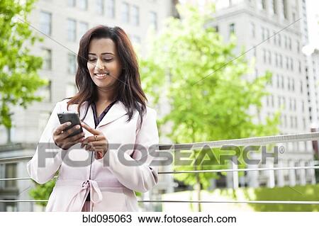 Stock Image - Indian businesswoman text messaging on cell phone. Fotosearch