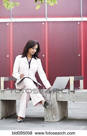 Stock Photo - Indian businesswoman using laptop on bench. Fotosearch
