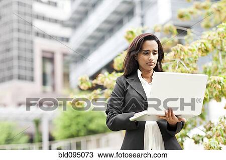 Stock Image - Indian businesswoman using laptop outdoors. Fotosearch
