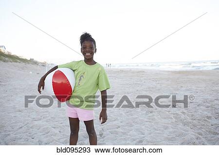 Stock Image - Jamaican girl holding ball on beach. Fotosearch