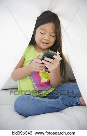 Stock Image - Korean girl using cell phone under sheet. Fotosearch