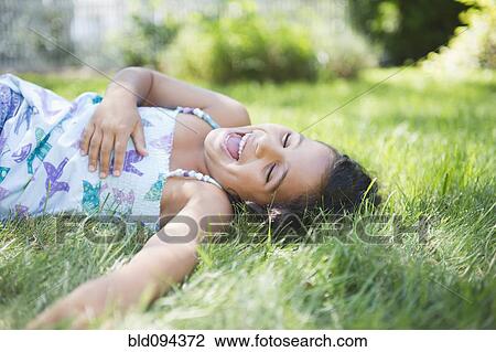 Stock Image - Laughing Hispanic girl laying in grass. Fotosearch