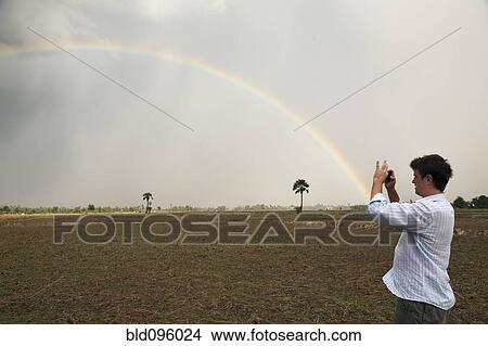 Picture - Man taking picture of rainbow. Fotosearch