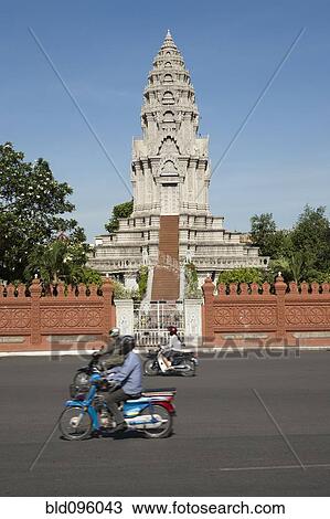 Stock Image - People on scooters near ornate temple. Fotosearch