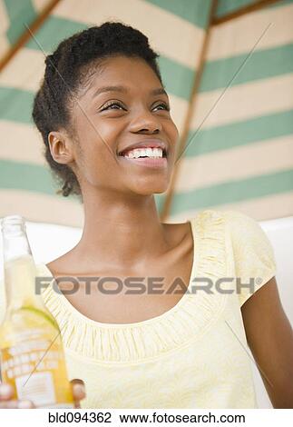 Stock Image - Smiling Black woman drinking beer. Fotosearch