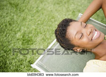 Stock Image - Smiling Black woman laying on deck chair . Fotosearch