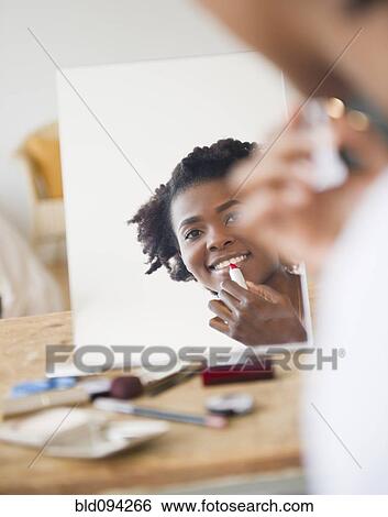 Stock Photograph - Smiling Black woman putting on lipstick. Fotosearch
