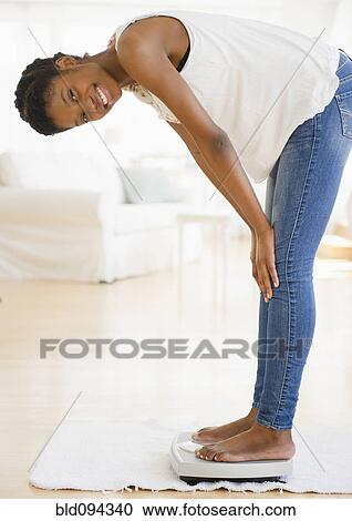 Smiling Black woman weighing herself View Large Photo Image Stock Image - Smiling Black woman weighing herself. Fotosearch