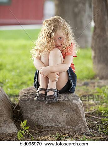 Stock Image - Smiling Caucasian girl sitting on rock. Fotosearch