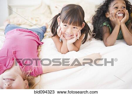 Smiling girls laying on bed together View Large Photo Image Stock Image - Smiling girls laying on bed together. Fotosearch