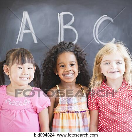 Picture - Smiling girls standing near blackboard. Fotosearch