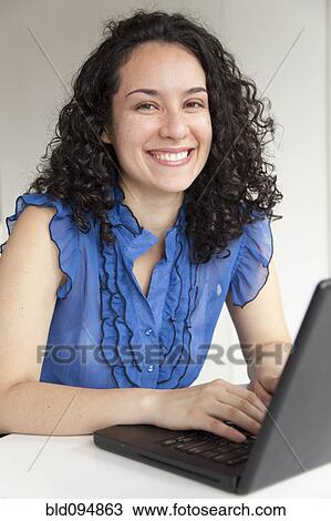 Stock Image - Smiling Hispanic businesswoman typing on laptop. Fotosearch