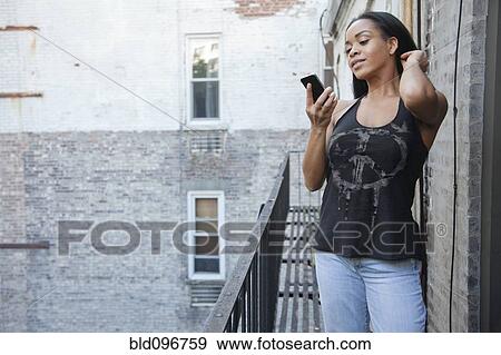 Stock Photo - African American woman using cell phone on fire escape. Fotosearch