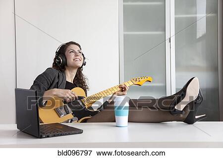 Stock Photo - Businesswoman playing guitar at desk. Fotosearch