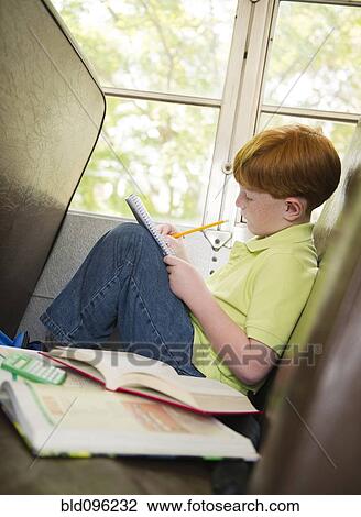 Stock Image - Caucasian boy doing homework on school bus. Fotosearch