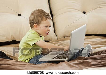 Caucasian boy using laptop on bed View Large Photo Image Stock Photo - Caucasian boy using laptop on bed. Fotosearch