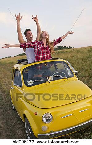 Stock Photo - Caucasian couple standing in car sun roof in field. Fotosearch