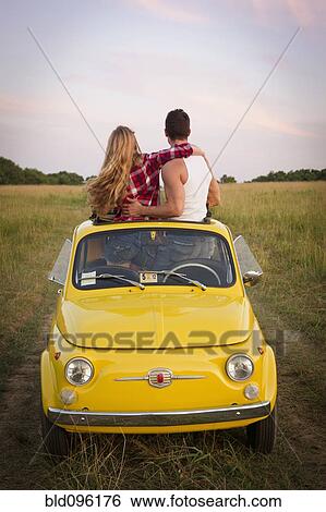 Stock Photograph - Caucasian couple standing in car sun roof in field. Fotosearch
