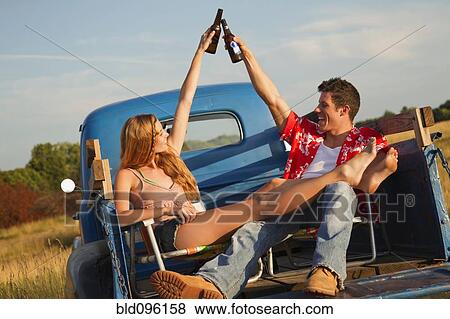 Stock Photo - Caucasian couple toasting with beer in back of truck. Fotosearch