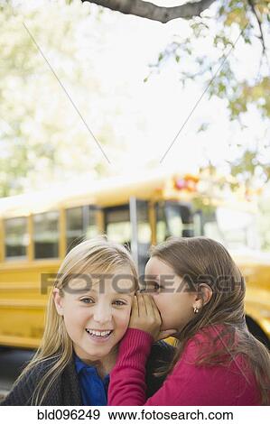 Stock Photo - Caucasian girls whispering while waiting for school bus. Fotosearch