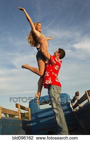 Stock Image - Caucasian man lifting girlfriend in back of truck. Fotosearch