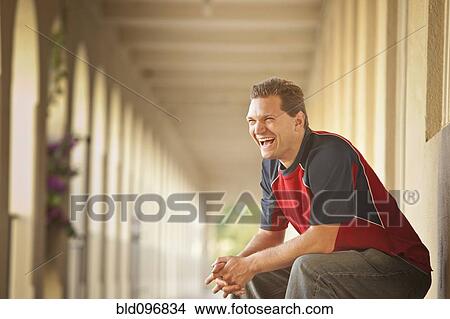 Picture - Caucasian man sitting outdoors laughing. Fotosearch