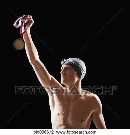 Stock Image - Caucasian teenage boy in swim cap and goggles holding medal. Fotosearch