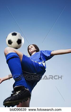 Stock Photo - Caucasian woman kneeing soccer ball. Fotosearch