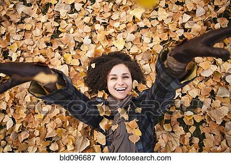 Stock Photo - Caucasian woman laying in autumn leaves. Fotosearch