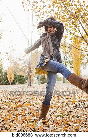 Stock Image - Caucasian woman playing in autumn leaves. Fotosearch