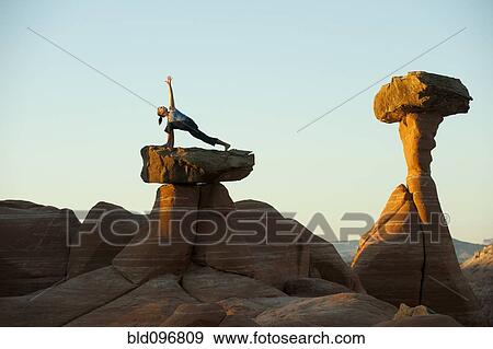 Stock Photo - Caucasian woman practicing yoga on top of rock formation. Fotosearch