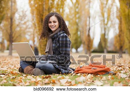 Stock Image - Caucasian woman using laptop in autumn leaves. Fotosearch