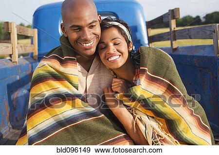 Stock Photo - Couple wrapped in blanket sitting on back of truck. Fotosearch