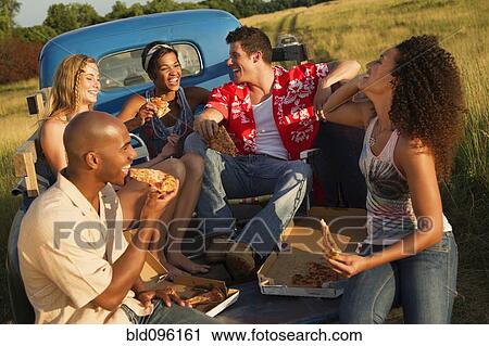 Stock Image - Friends eating pizza in back of truck. Fotosearch