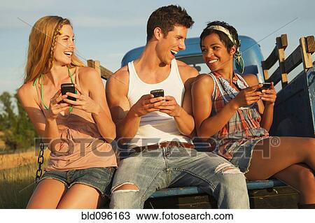 Stock Image - Friends using cell phones in back of truck. Fotosearch