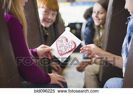 Stock Photography - Girl giving friend Valentine on school bus. Fotosearch