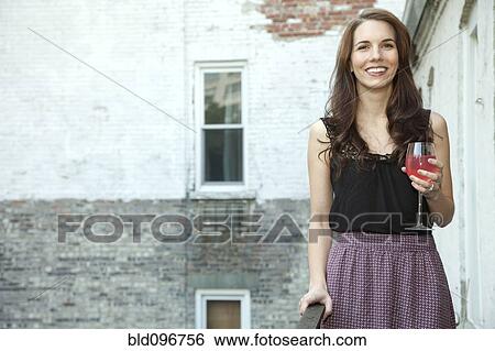 Stock Photograph - Glamorous Caucasian woman drinking wine on balcony. Fotosearch