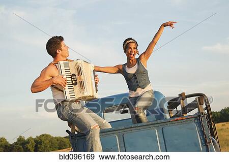 Stock Photo - Man playing accordion for girlfriend in back of truck. Fotosearch